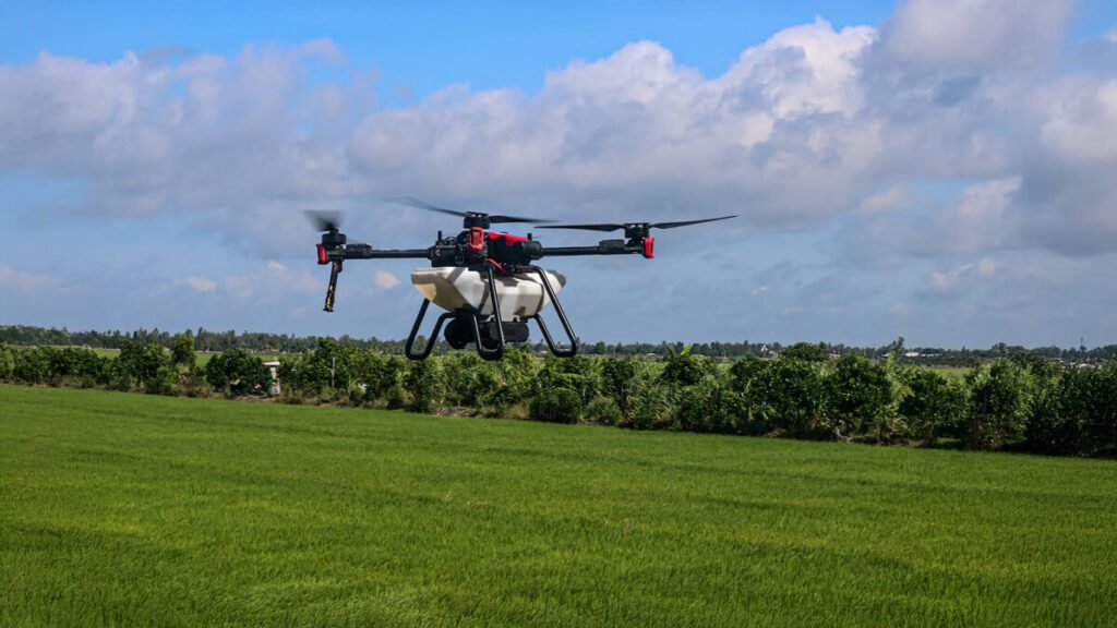Imagem de um drone agrícola pulverizando uma lavoura verde sob um céu azul com nuvens.